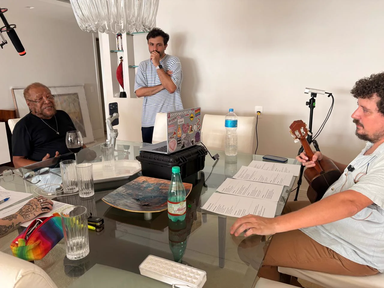 Martinho à mesa com a equipe, roteiro, instrumento, microfones e equipamentos de captura.